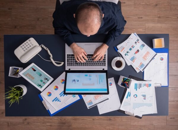 top-view-business-man-corporate-office-sitting-desk-typing-laptop-working-financial-statistics-business-strategy (1)