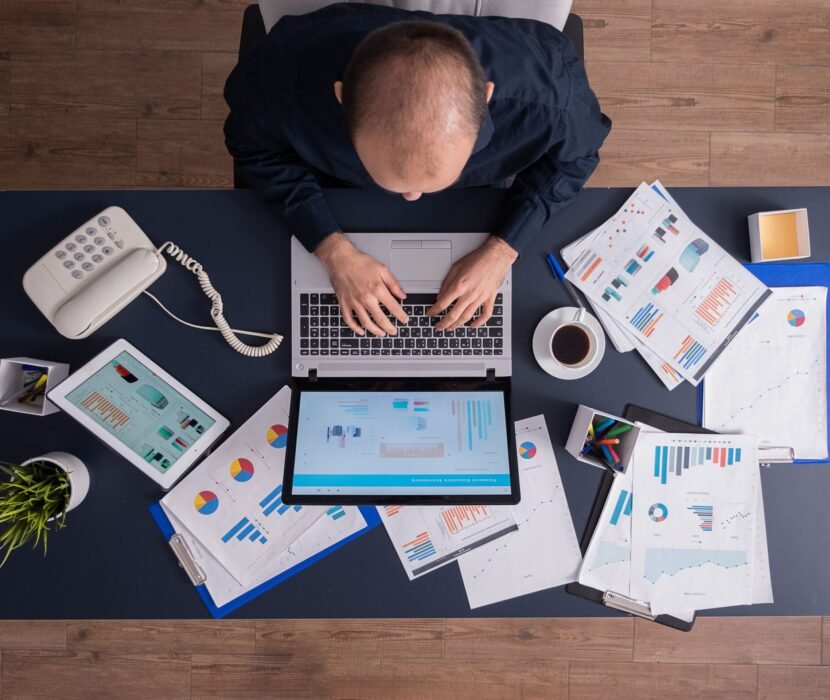 top-view-business-man-corporate-office-sitting-desk-typing-laptop-working-financial-statistics-business-strategy (1)